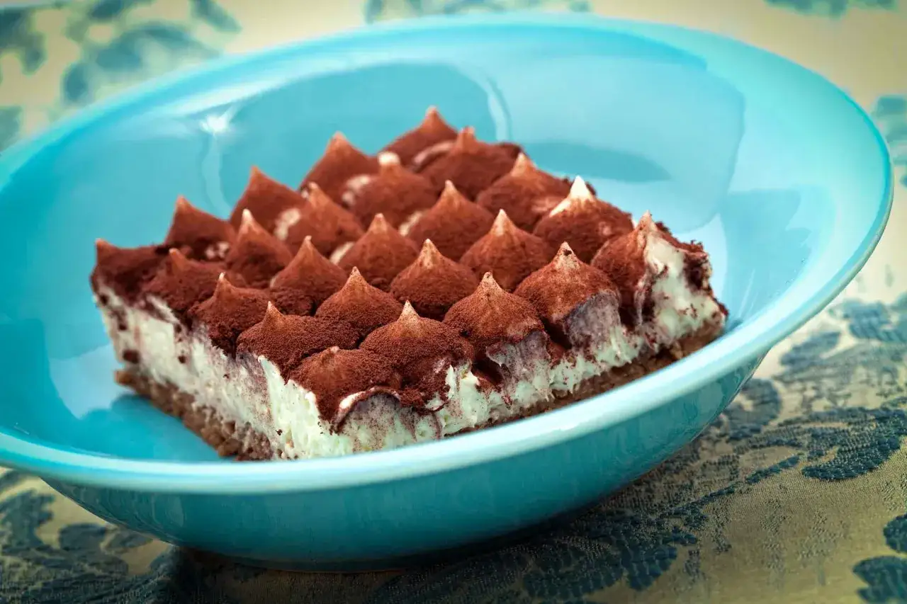 Un d&eacute;licieux tiramisu cacao, parsem&eacute; de poudre de cacao, repose dans un plat bleu vif.
