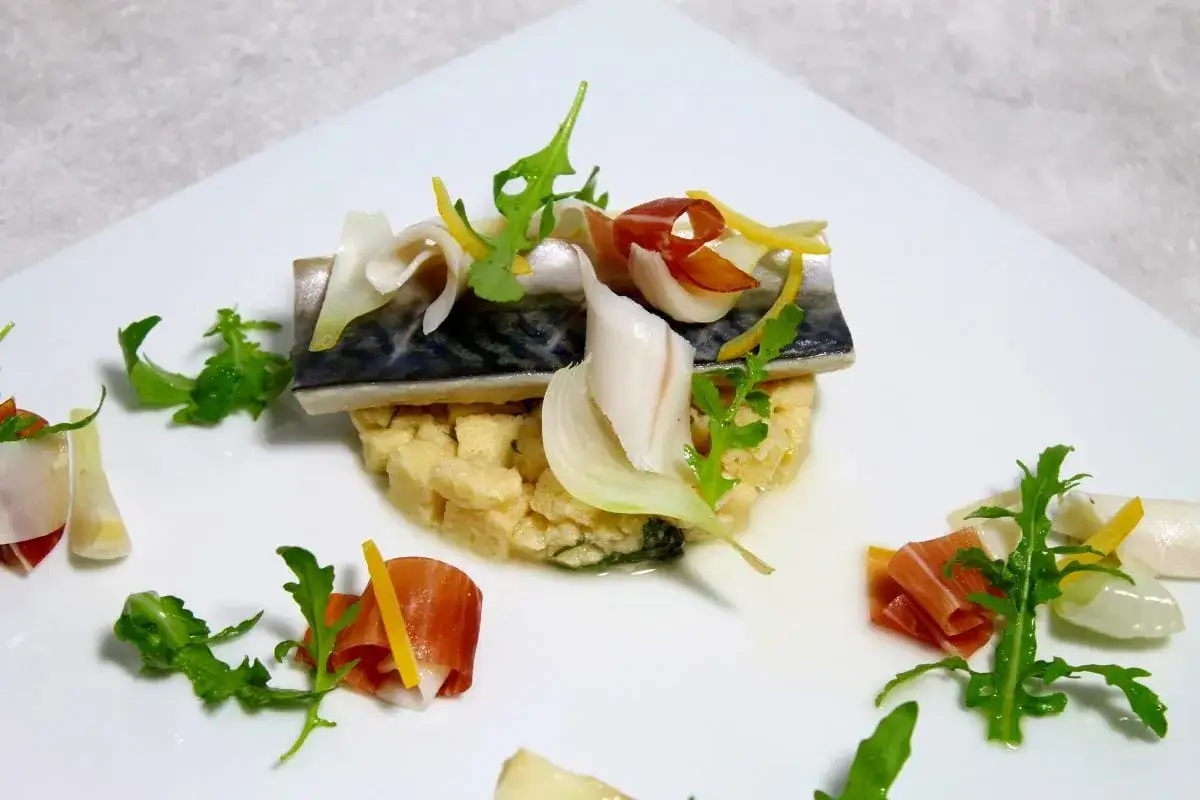 Un d&eacute;licieux maquereau au vin blanc, servi sur un lit de semoule, garni de fines lamelles de jambon cru, d'oignon et de roquette.