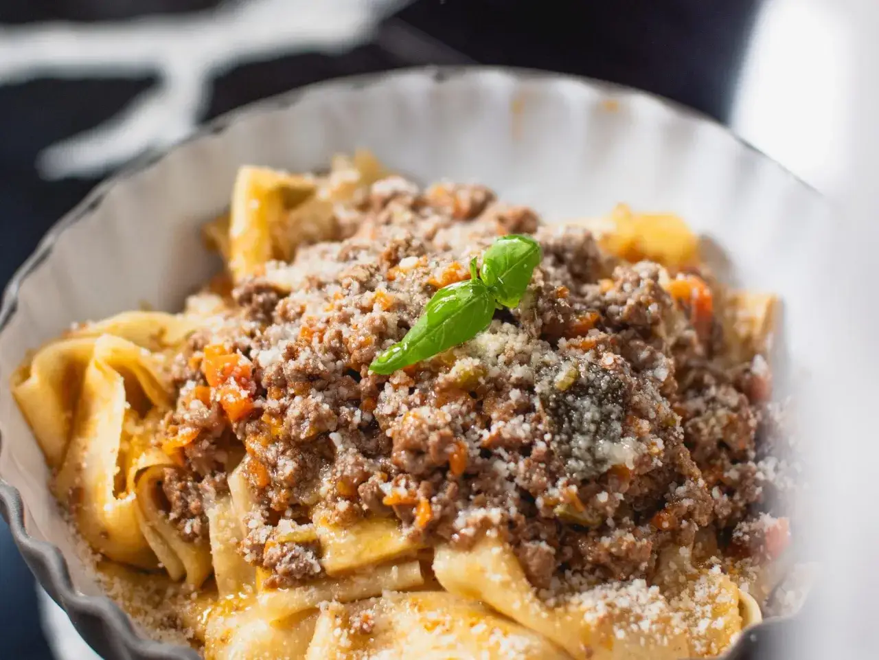 Un plat de pâtes fraîches, garni d'une sauce bolognaise riche et savoureuse, parsemé de parmesan et d'une feuille de basilic. Une invitation à la recette spaghetti bolognaise italienne.