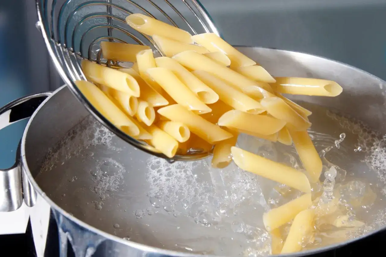 P&acirc;tes penne tombant dans l'eau bouillante pour la cuisson. Le bruit de l'eau qui &eacute;clabousse annonce le d&eacute;but du repas.