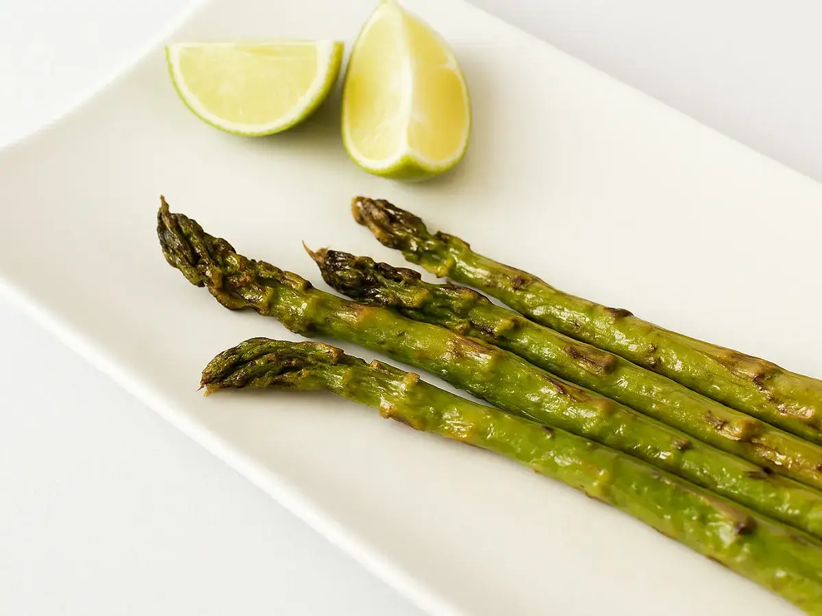 Asperges au four, légèrement grillées, servies sur une assiette blanche avec des quartiers de citron vert.