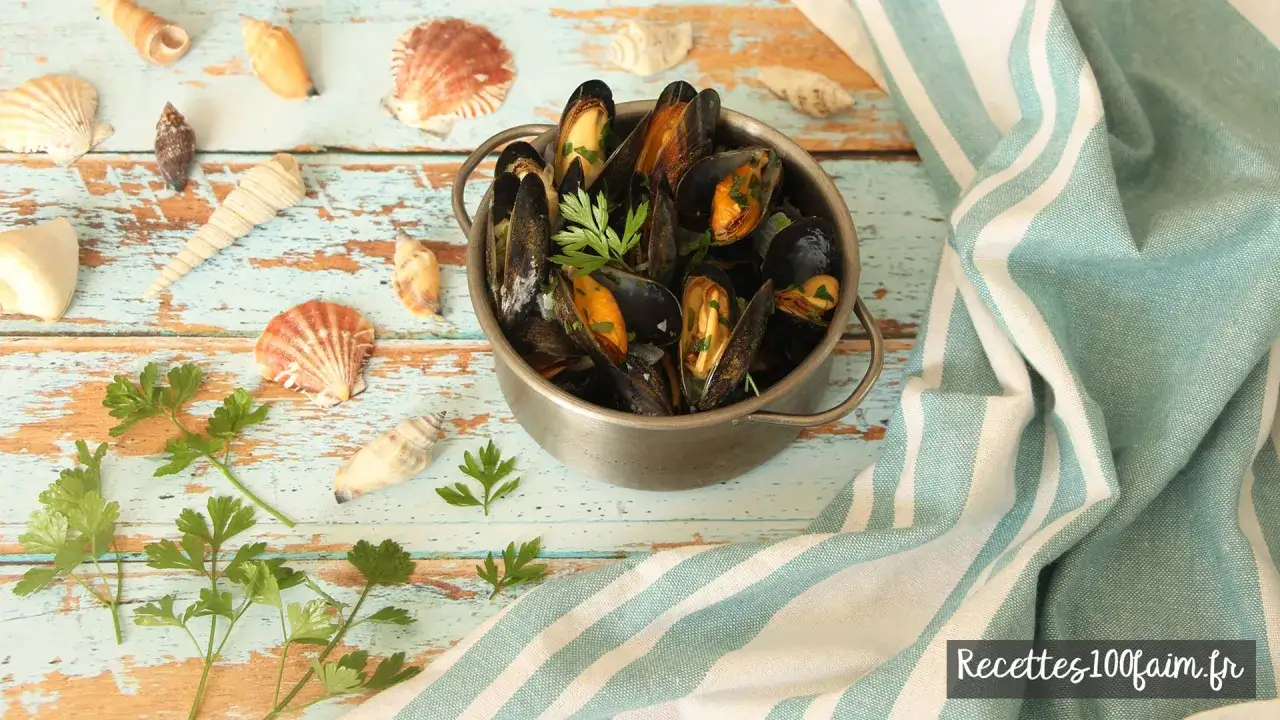 Un plat de moules marini&egrave;res fumantes, garni de persil frais, entour&eacute; de coquillages sur une table en bois patin&eacute;.