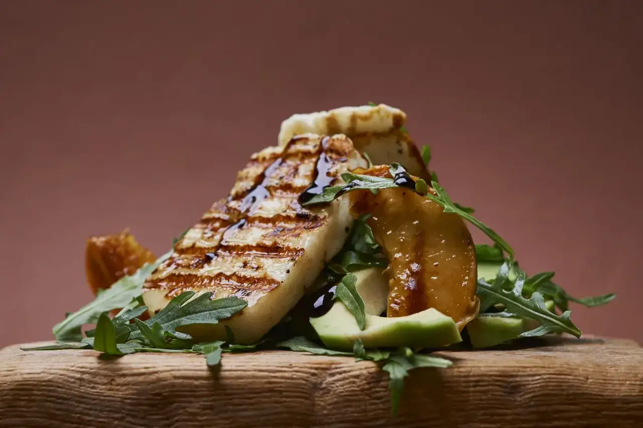 Tranches de halloumi grill&eacute;, arros&eacute;es de sauce, sur un lit de roquette et d'avocat, avec des morceaux de fruits caram&eacute;lis&eacute;s.