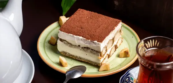 Un tiramisu onctueux, saupoudré de cacao, servi avec des morceaux de fruits. Une idée pour par quoi remplacer le café dans le tiramisu ?